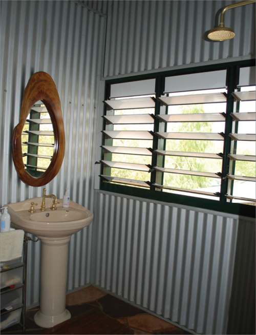 An open-plan bathroom with a shower and hand basin has three louvred windows to allow natural light and airflow.