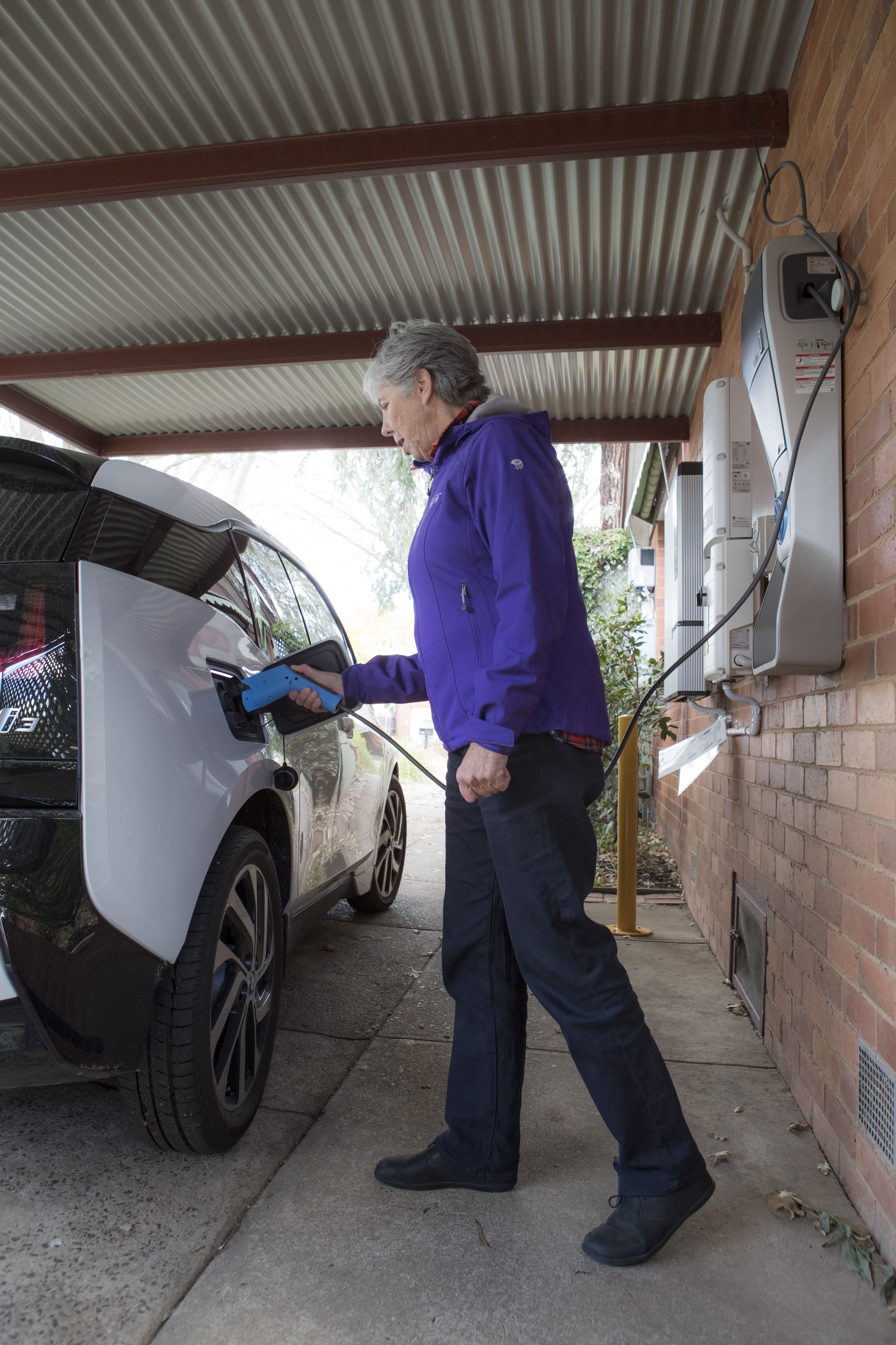 A lady plugs a corded electric charger into her electric car.