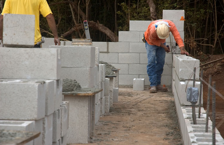 A photograph of a builder constructing a wall using concrete blocks. 