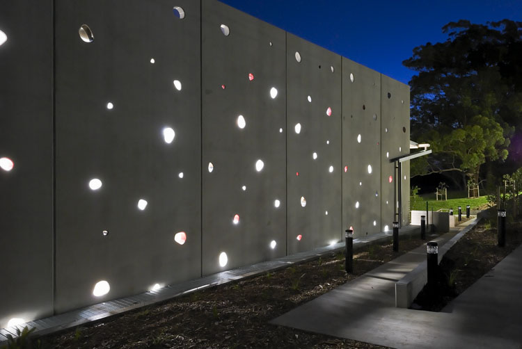 A photo of the outside of a pre-cast concrete wall with many irregular-shaped and differently sized windows.