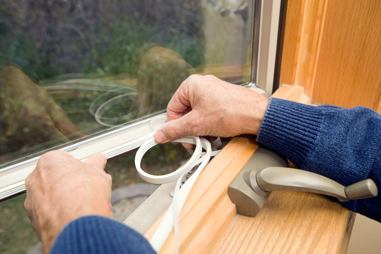 A photograph of a persons hands installing a weather strip around a window frame.